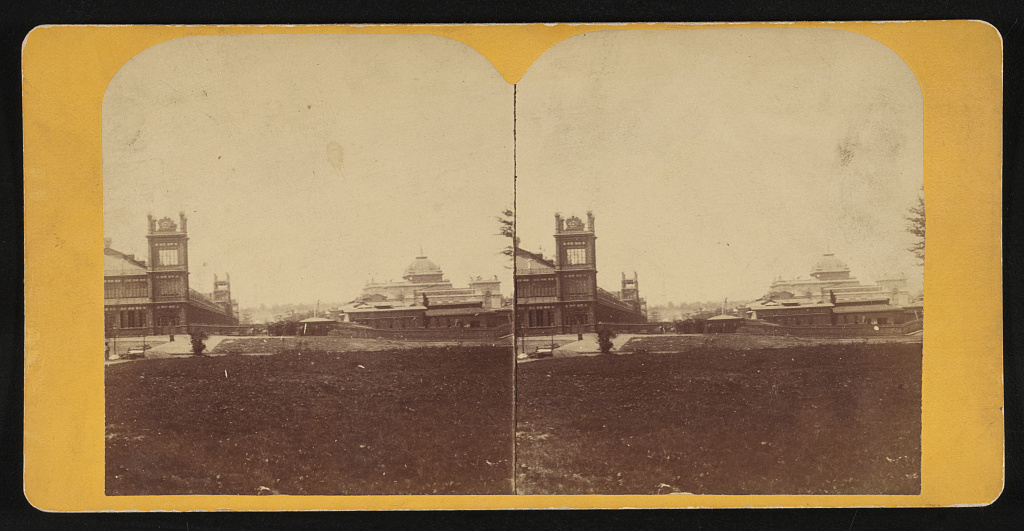 A yellow stereo card shows a long building with square ornamental towers at left and a pale domed hall at right, partly hidden behind low roofs.